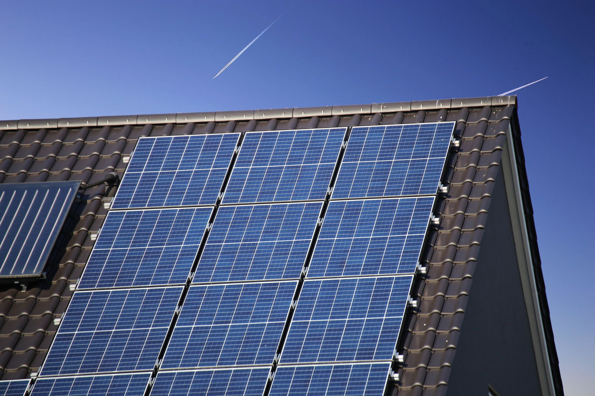 Photovoltaikmodule auf einem dunklen Ziegeldach vor blauem Himmel